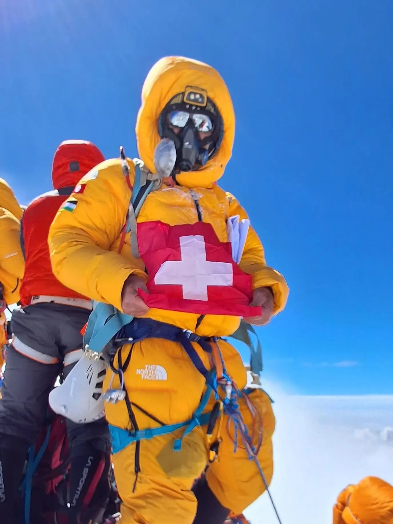 Ziad au sommet de l’Everest, en combinaison d’altitude et masque à oxygène, drapeau suisse en main
